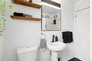 Bathroom featuring a sink, a wainscoted wall, updated fixtures and shelving.