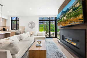 Living area with recessed lighting, light wood-style flooring, a glass covered fireplace, and a wall of windows