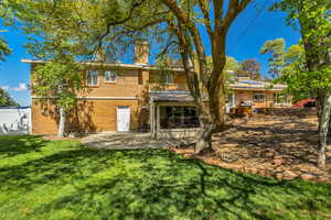 Back of house featuring a chimney, a lawn, brick siding, roof mounted solar panels, and a patio