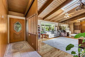 Foyer entrance featuring baseboards, a ceiling fan, vaulted ceiling with skylight, and wooden ceiling
