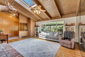 Living room with vaulted ceiling with skylight, a ceiling fan, light wood-type flooring, visible vents, and wood ceiling