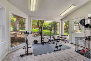 Workout area featuring baseboards, plenty of natural light, light tile patterned floors, and lofted ceiling
