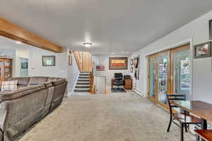 Carpeted living room with a textured ceiling, stairs, baseboards, a baseboard radiator, and beamed ceiling