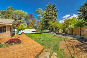 View of yard featuring a deck, a fenced backyard, and a trampoline