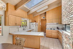 Kitchen featuring light tile patterned flooring, white appliances, vaulted ceiling with skylight, tasteful backsplash, and a sink