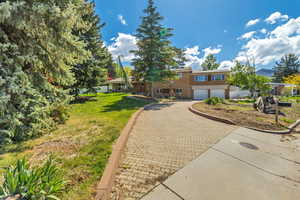 View of front of home with an attached garage, a front lawn, and decorative driveway