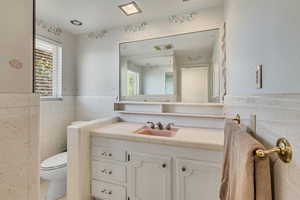 Bathroom featuring vanity, visible vents, wainscoting, toilet, and tile walls