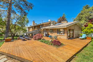 Back of house with brick siding, outdoor dining area, a wooden deck, and a chimney