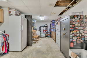Interior space with white fridge with ice dispenser, unfinished concrete flooring, and a paneled ceiling