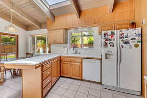 Kitchen with wood ceiling, tile countertops, a sink, a peninsula, and white appliances