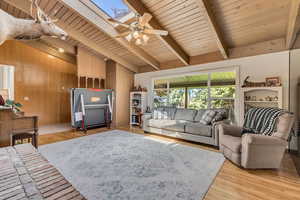 Living room with wood ceiling, ceiling fan, wood walls, light wood finished floors, and lofted ceiling with skylight