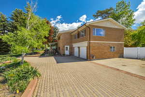 View of side of property featuring fence, an attached garage, driveway, and brick siding