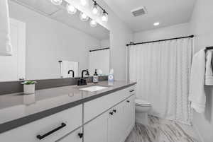 Full bath featuring visible vents, vanity, marble finish floor, curtained shower, and toilet