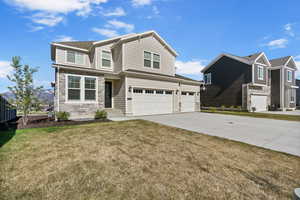Traditional home with a garage, a front yard, driveway, and stone siding