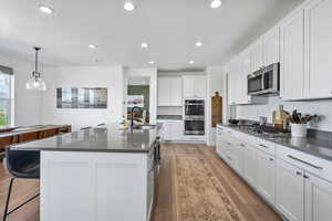 Kitchen with appliances with stainless steel finishes, dark countertops, a sink, light wood finished floors, and white cabinetry
