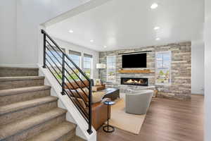 Living room featuring a stone fireplace, wood finished floors, stairway, baseboards, and recessed lighting