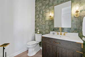 Bathroom featuring vanity, wood finished floors, toilet, tile walls, and baseboards