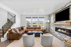Living area with recessed lighting, a stone fireplace, wood finished floors, and stairway