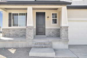 Property entrance with a porch, a shingled roof, stone siding, and stucco siding