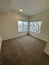 Unfurnished room with baseboards and dark colored carpet