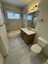 Bathroom featuring a healthy amount of sunlight, toilet, shower / tub combination, and marble finish floor