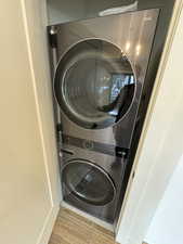 Clothes washing area featuring laundry area, stacked washing maching and dryer, and wood finished floors