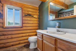 Bathroom featuring vanity, log walls, a wealth of natural light, and toilet