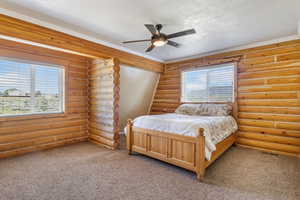 Bedroom with rustic walls, light colored carpet, and multiple windows