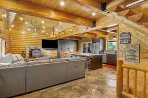 Living area featuring a wood stove, rustic walls, beam ceiling, and wooden ceiling