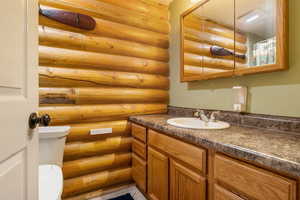 Full bath with log walls, vanity, and toilet