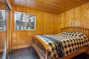Bedroom with finished concrete floors, wood ceiling, wooden walls, and multiple windows