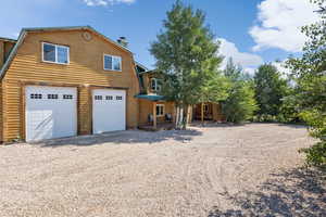 View of front of property featuring a gambrel roof, a garage, a chimney, covered porch, and gravel driveway