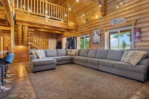 Living room with stairs, a towering ceiling, rustic walls, and wood ceiling