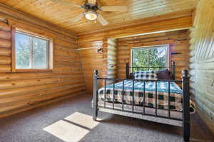 Carpeted bedroom featuring wood ceiling, rustic walls, and a ceiling fan