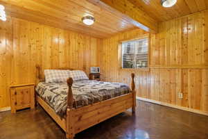 Bedroom featuring baseboards, wood walls, concrete flooring, and wooden ceiling