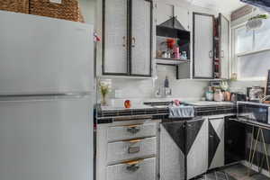 Kitchen with light countertops, decorative backsplash, freestanding refrigerator, and ornamental molding