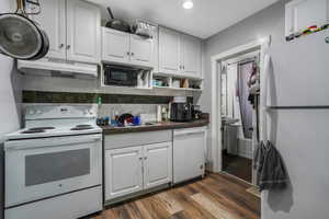 Kitchen featuring dark countertops, white appliances, under cabinet range hood, a sink, and dark wood finished floors