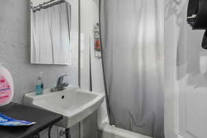 Full bath featuring a sink, a textured wall, and shower / tub combo