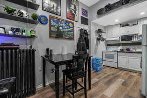 Kitchen featuring dark countertops, white cabinets, radiator heating unit, white appliances, and dark wood-type flooring
