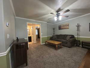 Carpeted living room featuring crown molding, a ceiling fan, and baseboards