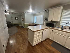 Kitchen with dark wood-style flooring, a peninsula, stainless steel microwave, a sink, and dishwasher