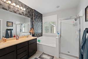 Bathroom featuring a sink, double vanity, wallpapered walls, a bath, and a stall shower