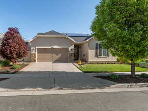 Ranch-style home featuring driveway, solar panels, a front yard, an attached garage, and stucco siding