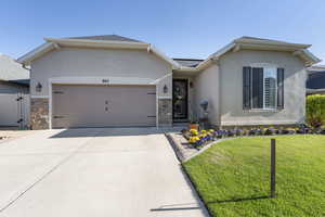 Single story home with stone siding, an attached garage, stucco siding, a front lawn, and driveway
