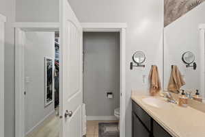 Bathroom featuring a walk in closet, vanity, baseboards, tile patterned floors, and toilet