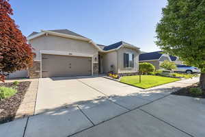 Single story home with an attached garage, stucco siding, solar panels, a front yard, and driveway
