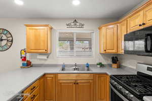 Kitchen featuring stainless steel range with gas cooktop, a sink, black microwave, and light countertops
