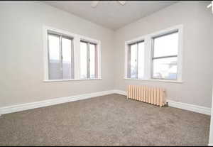 Carpeted empty room with a ceiling fan, baseboards, and radiator heating unit