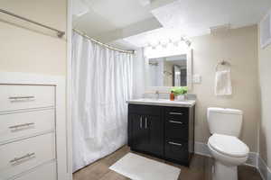 Bathroom featuring a shower with curtain, visible vents, wood finished floors, vanity, and toilet