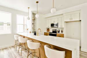 Kitchen featuring light wood-style flooring, stainless steel appliances, a breakfast bar, and white cabinetry